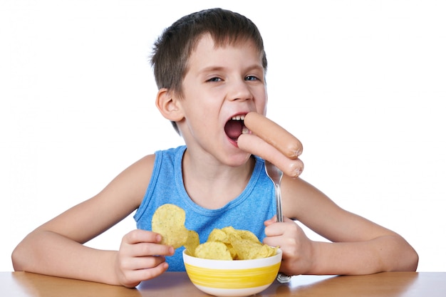 Photo little boy eating sausages and potato chips isolated