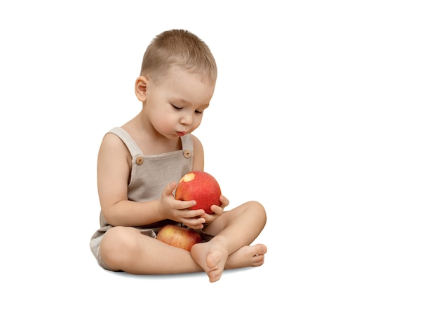 A little boy eats an apple sitting on the floor