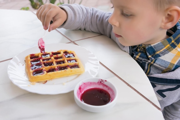 A little boy eats dessert Belgian waffles with jam in a cafe