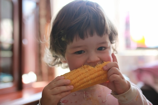 小さな男の子は貪欲に噛むトウモロコシの穀物を食べる