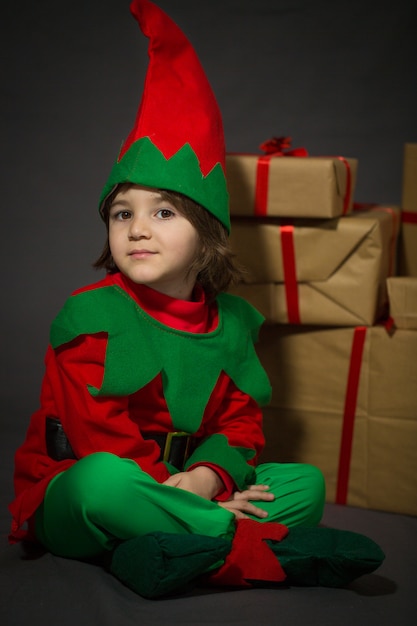 Photo little boy in elf dress sitting near a gift boxes