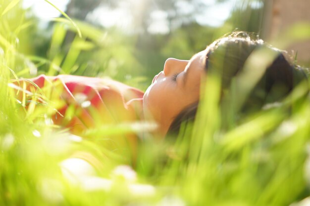 Little boy enjoying summer time lying on meadow green grass with sunbeam in his hair