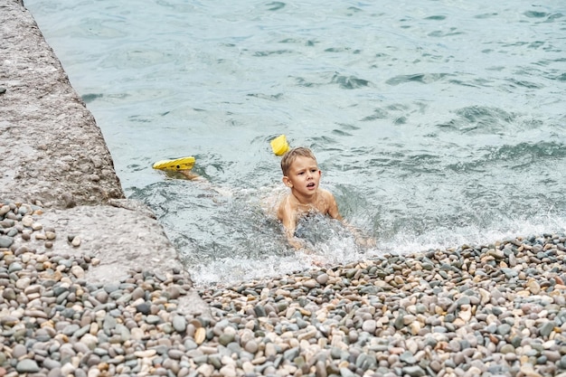 Little boy enjoys swimming in shallow sea water with pebble bottom