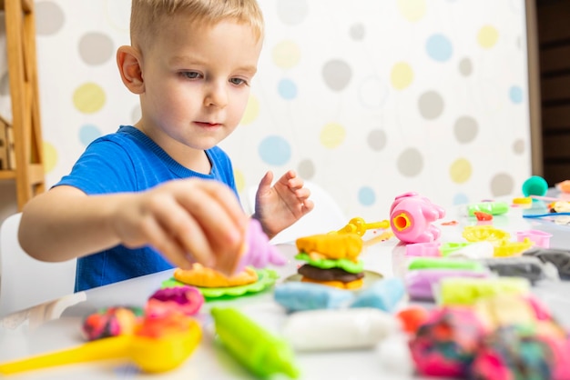 写真 小さな男の子は熱心に白いテーブルの上でプラスチリンでプレイドッグをします