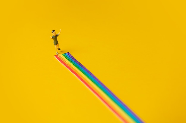 小さな男の子の図は、黄色の背景に虹のLGBTストリップの上に立っています