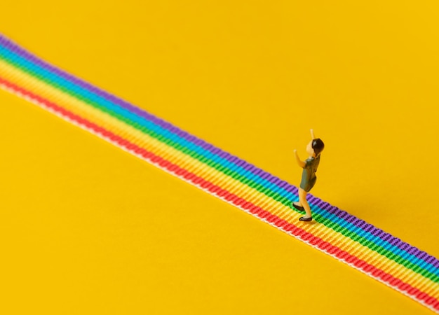 Little boy figure stand on rainbow LGBT strip on yellow background