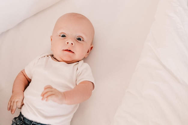 小さな男の子面白いかわいい子赤ちゃんベッドに横たわって、カメラを見てします。遊び心のある幼児