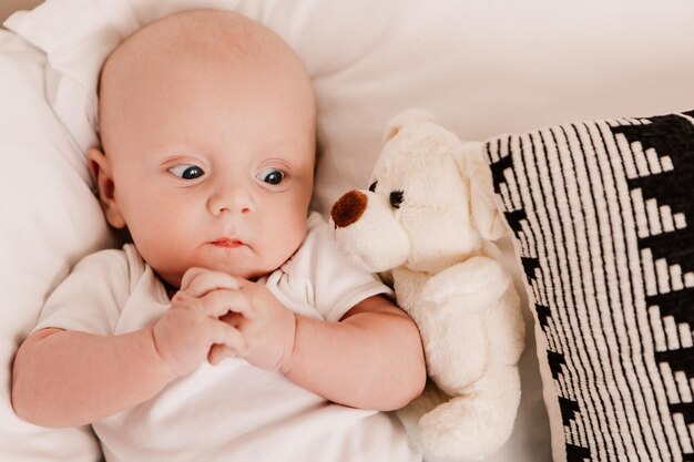 어린 소년은 푹신한 장난감을 가지고 침대 베개에 누워 있는 재미있는 귀여운 아기입니다. 장난기 많은 유아