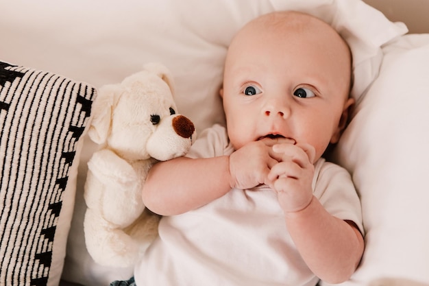 Little boy funny cute child baby lying on bed pillows with fluffy toy. Playful toddler