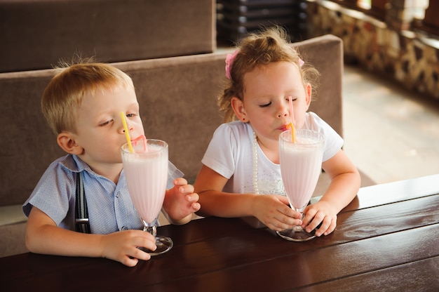 Little boy and girl drinking milkshakes in a cafe outdoors.