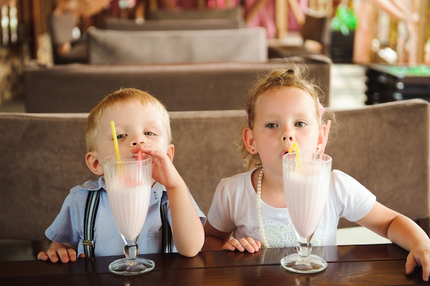 Little boy and girl drinking milkshakes in a cafe outdoors.