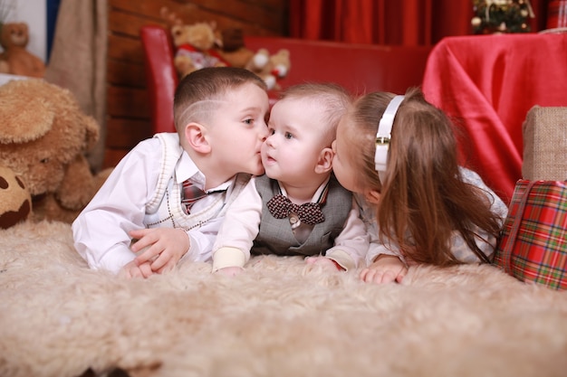 Ragazzino e ragazza che baciano il loro fratellino e si trovano vicino a regali di un albero di natale. vacanze di capodanno. famiglia, felicità, vacanze, concetto di natale.