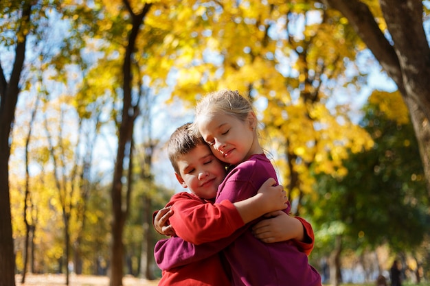 Little boy and girl in a park in autumn. Boy hugging a girl