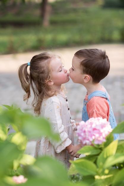 маленький мальчик и девочка стоят, держась за руки и целуются в День святого Валентина