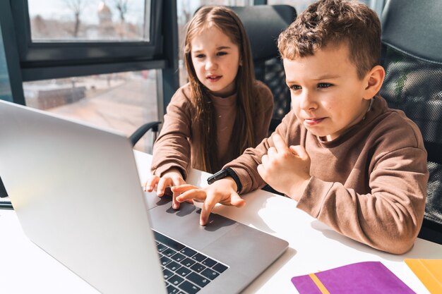 Little boy and girl study online in home at the laptop