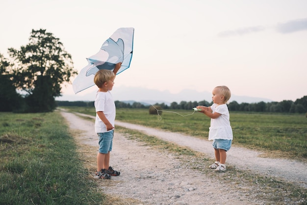 Little boy and girl with kite on nature in countryside Family outdoors Children playing on meadow on sunset Photo of leisure dreams summer holidays family values sustainable lifestyle