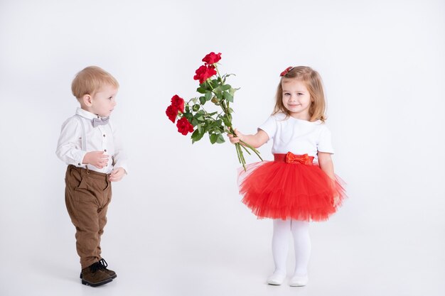 Little boy giving bouquet of roses to toddler girl on valentines day on white wall.