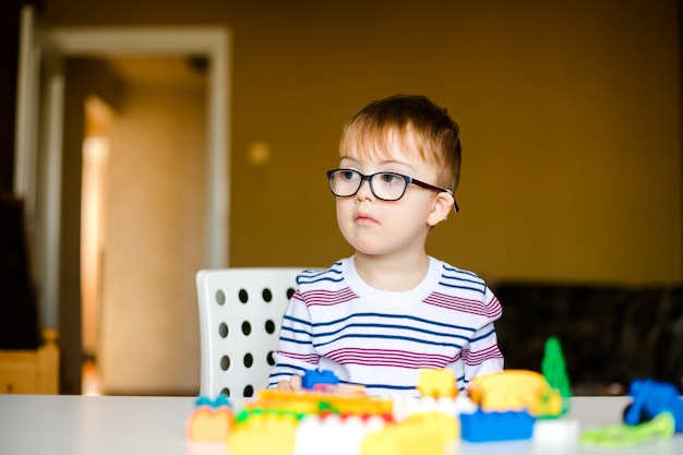 Маленький мальчик в очках с синдромом рассвета, играя с разноцветными кирпичами