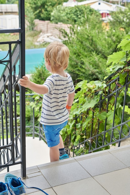 A little boy goes down the stairs to the garden. The child goes down the stairs.