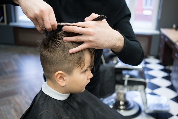 Ragazzino su un taglio di capelli nel barbiere si siede su una sedia.