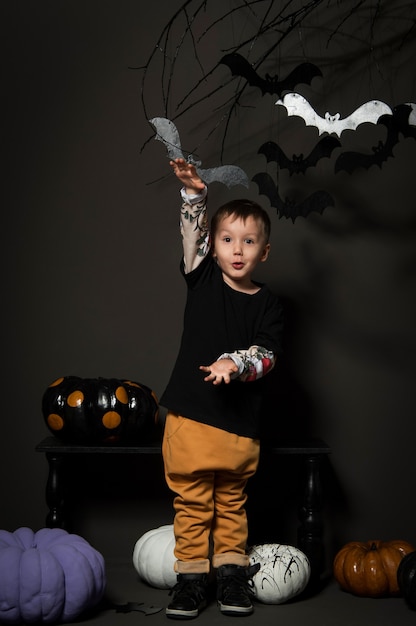 Маленький мальчик на хэллоуин на черном фоне с тыквами и летучими мышами на дереве