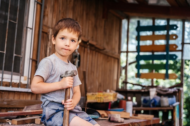 Little boy hammers nails with a hammer in a wooden board in the carpenter's workshop