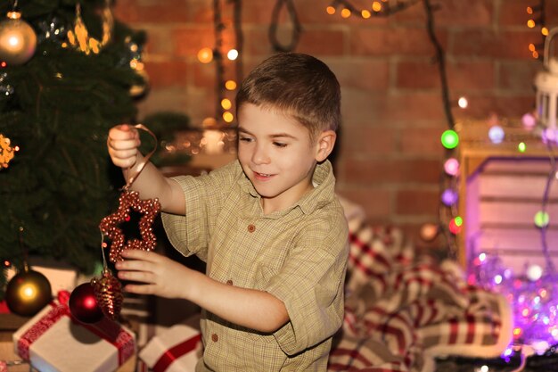 クリスマスの表面上のモミの木におもちゃをぶら下げている小さな男の子