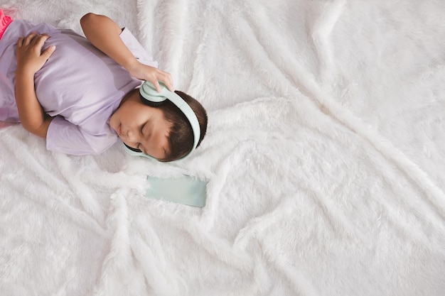 The little boy happily lies down and listens to music with headphones.