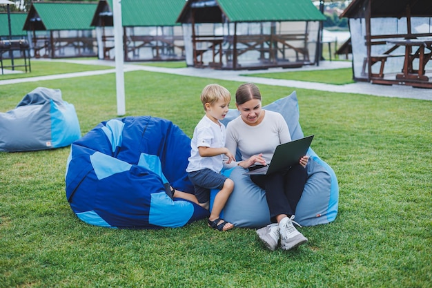 Little boy having fun sitting on sack in summer or spring in\
park outdoors family vacation of mother and son in the fresh\
air