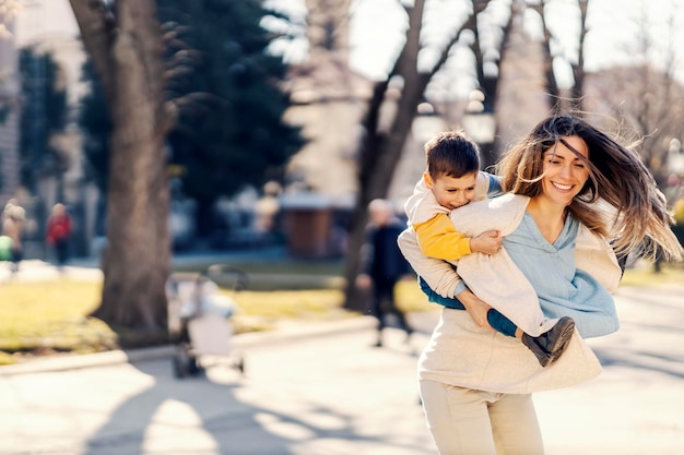 A little boy having piggyback ride and spinning with mother in a park