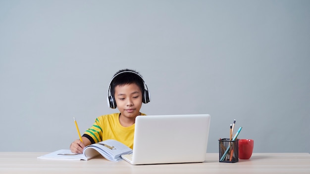 Ragazzino in cuffie che studiano in linea facendo uso del computer portatile