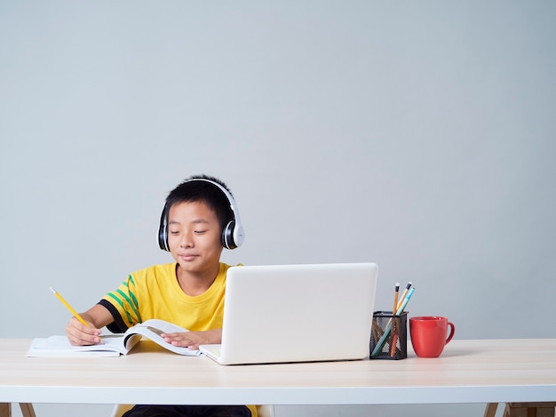 Маленький мальчик в наушниках учится онлайн с помощью ноутбука