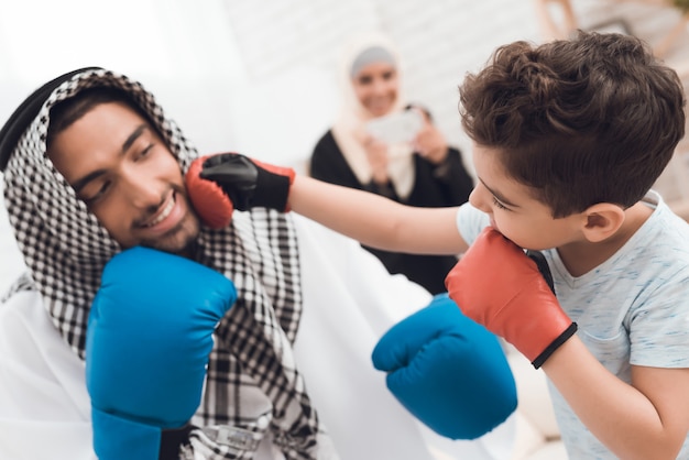 Photo little boy and his father in clothes train in boxing gloves.