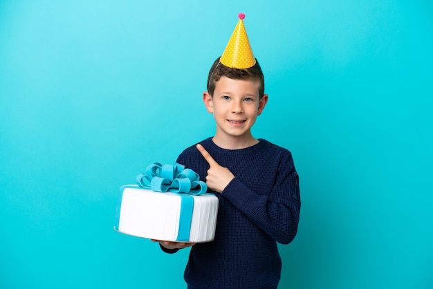 Ragazzino che tiene la torta di compleanno isolata su sfondo blu che indica il lato per presentare un prodotto