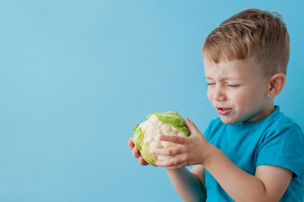 Little Boy Holding Broccoli in his hands on blue background, diet and exercise for good health concept