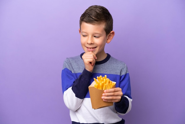 Ragazzino che tiene patatine fritte isolate su sfondo viola guardando di lato e sorridente