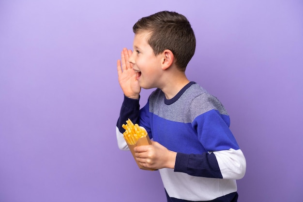 Little boy holding fried chips isolated on purple background shouting with mouth wide open to the side