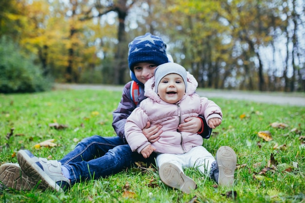 草の上に座って、彼の妹を腕に抱いて小さな男の子