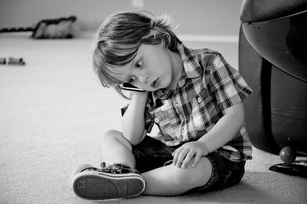 Photo little boy holding mobile phone to ear while sitting on floor