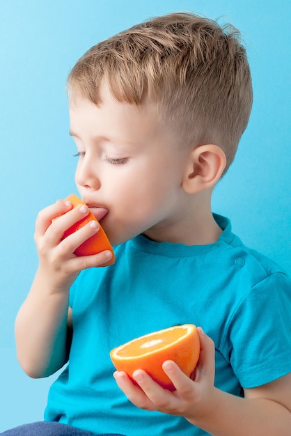 Little Boy Holding an Orange in his hands on blue background, diet and exercise for good health concept