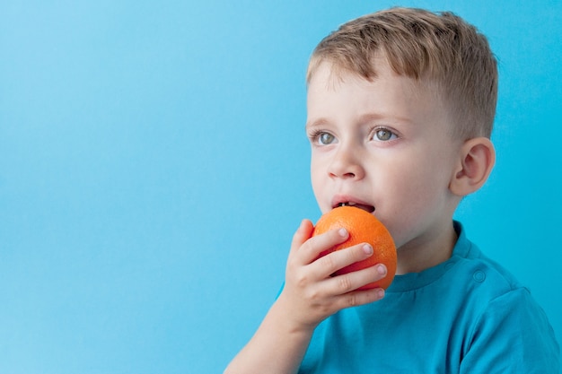 青い壁にオレンジを手に持って、ダイエットと健康コンセプトを行使する小さな男の子