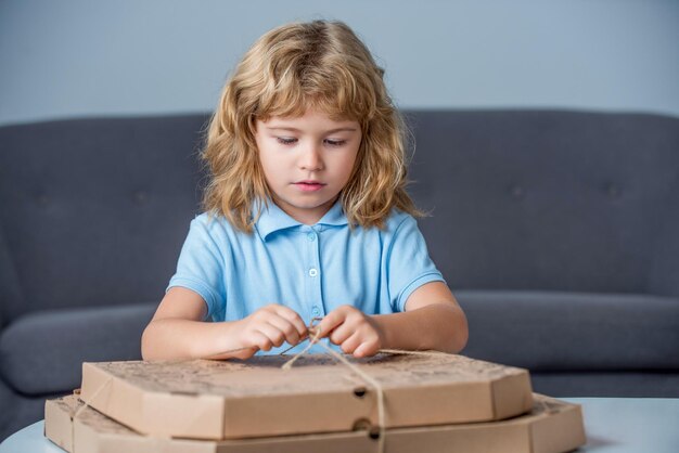 Little boy holding pizza boxes Boy ready to eat a pizza Little child looking at a pizzas box Child is astonished by a big box with a huge pizzas very surprised and happy