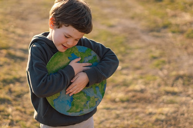 Little boy holding planet in hands against green spring background earth day