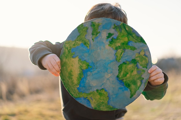 Little boy holding planet in hands against green spring background earth day