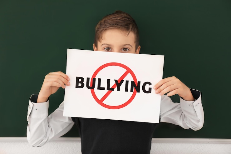 Photo little boy holding sign with crossed word bullying in classroom