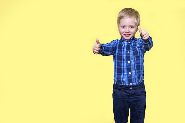 Little boy holding thumbs up and smiling yellow background with space for text