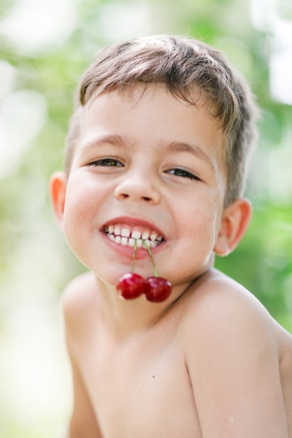 小さな男の子は彼の歯にさくらんぼを持っています