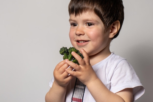 A little boy holds a green broccoli in his hands sniffs it and smiles