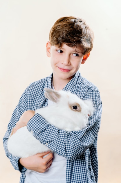 Маленький мальчик держит кролика в его руках на изолированном свете