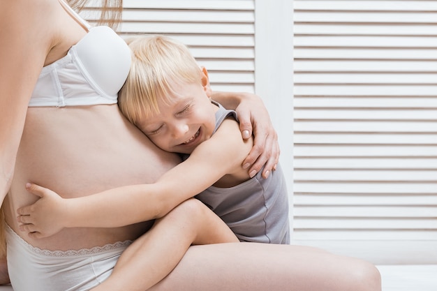 Little boy hugging his stomach of pregnant mother and laughs. young pregnant woman and the eldest son